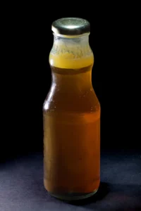 Chai thủy tinh đựng mật ong vàng sẫm, nắp kim loại, không nhãn, trên nền đen